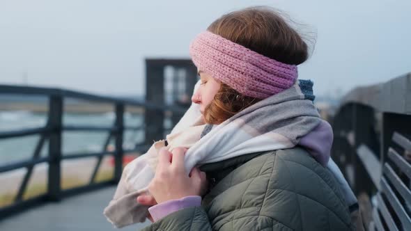 Woman in Warm Clothes Wraps Up in the Scarf at the Winter Sea Coastline