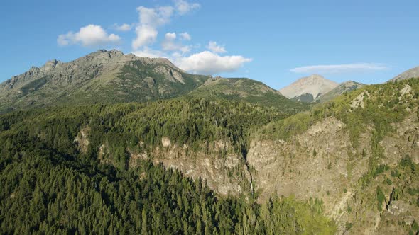 Aerial dolly out rising over mountains covered in pine tree forest and Corbata Blanca waterfall in b