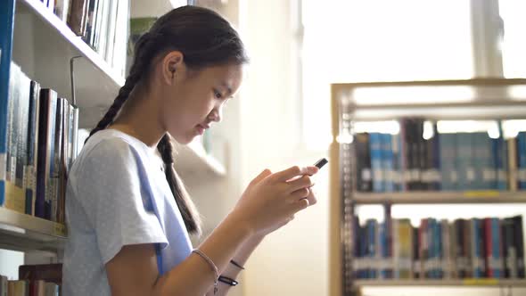 Asian teenager student using smart phone in school library.