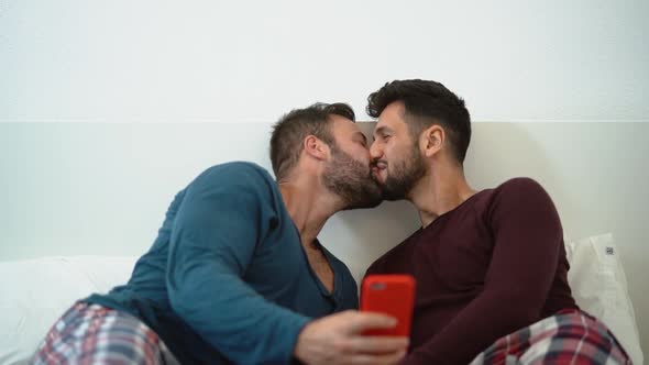 Happy gay men couple using mobile phone in bed