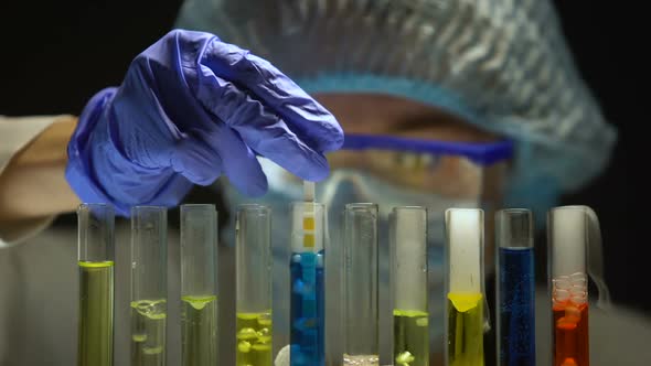 Scientist Measuring Acidity Level in Tube With Blue Liquid in Dark Laboratory