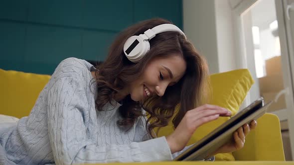 Girl with Headphones Listening Music and Using Pad, Laying on the Light-Green Couch