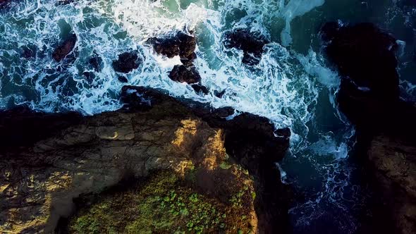 Rising aerial shot of waves crashing into a rocky cove on the California coast