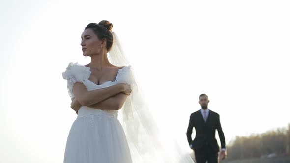 Beautiful Bride in a Chic White Dress Is Standing in Field, Looking To the Side and Waiting for Her