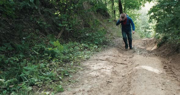 Hiker in a Cowboy Hat Walks a Steep Slope in the Middle of a Summer Forest