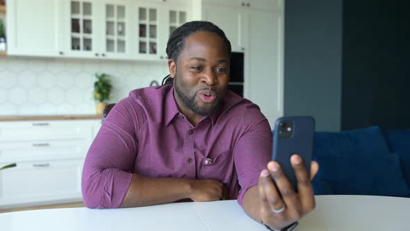 Positive and Joyful AfricanAmerican Guy Makes Video Call By the Smartphone