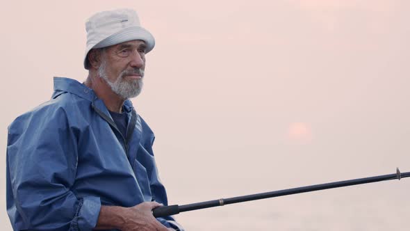 Old fisherman standing on sea side rocks and fishing against the sunset