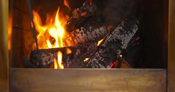 A Person Straightens a Log in the Fireplace with a Iron Poker