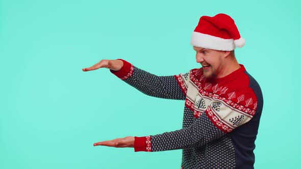 Man Wears Red New Year Sweater Deer Showing Thumbs Up and Pointing at on Blank Advertisement Space