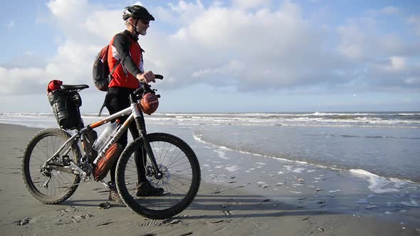 A man standing on the beach next to his mountain bike.