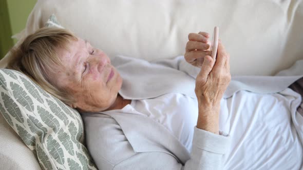 Grandmother Relaxing On Sofa Using Smartphone