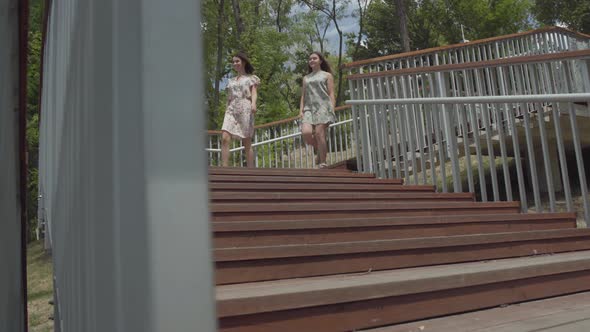 Two Cute Young Woman Wearing Summer Dresses Running Down the Stairs in the City Park