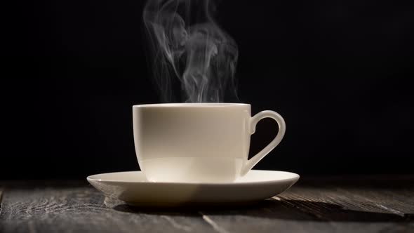 Cup of Hot Coffee, Steam Coming Out of a Coffee Cup Standing on a White Saucer on a Wooden Table