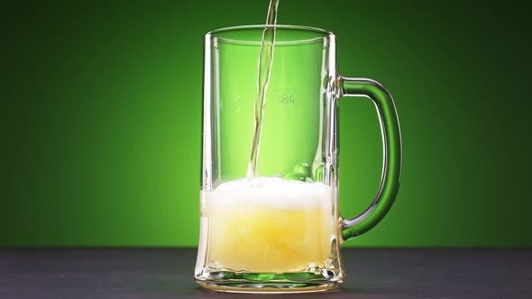 Beer Slowly Pours Into a Glass on Green Background