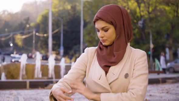 A Young Beautiful Muslim Woman Adjusts Her Clothes in a Street in an Urban Area