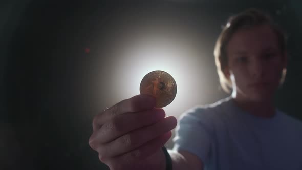 A Young Man is Holding a Bitcoin in His Hand Through Which the Light Shines Through