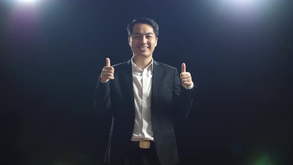 Smiling Asian Speaker Man In Business Suit Showing Thumbs Up Gesture To Camera While Standing