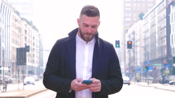 Slow motion of young bearded man outdoor holding smartphone looking camera smiling