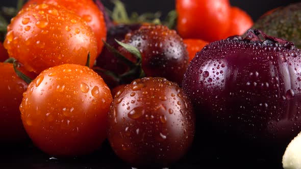 Cherry tomatoes, cucumbers, garlic, avocado and red onion on a black background in water drops