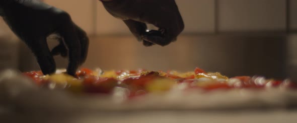 Chef placing colorful cherry tomatoes on a fresh pizza dough. Slow motion, close up.