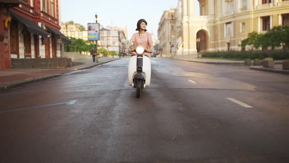 Young Beautiful Girl Riding Around City on Scooter at Sunrise