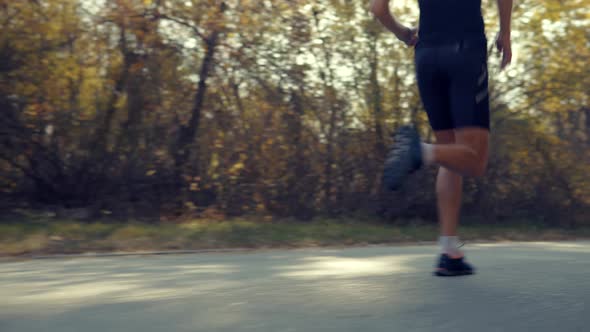 Running Man In Forest At Sunset. Runner Man Fit Athlete Legs Jogging On Trail Ready To Triathlon.