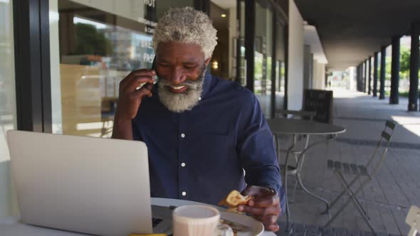 African american senior man talking on smartphone while having breakfast sitting outdoors at cafe