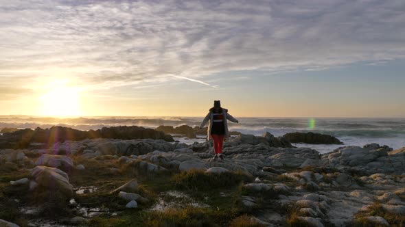 Mature Senior Caucasian Woman Walking Forward in Down Jacket Hat Beanie at the Sea with Slow Waves