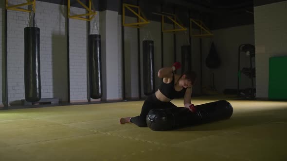 Kickboxing Aggressive Woman Fighter Trains His Punches Beats a Punching Bag While Lying on the Floor