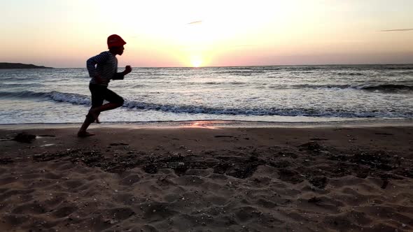 Silhouette of Boy Running Along Seashore in Evening at Sunset Slow Motion Video