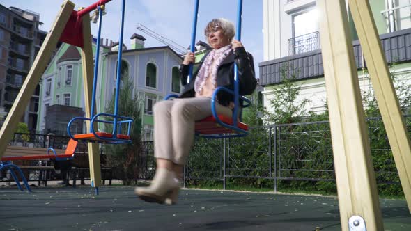 Wide Shot Sad Senior Lonely Woman Swinging on Swings on Playground on Sunny Day Outdoors