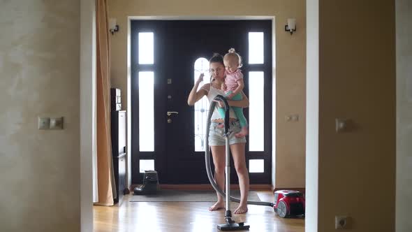 young mother vacuuming the floor in the hallway of the house with a small child