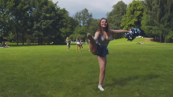 Beautiful Cheerleader in Uniform Practicing Split Holding Pompom Standing Outdoors