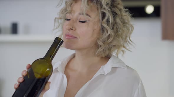 Closeup Portrait of Gorgeous Confident Woman Smelling Wine Bottle Smiling and Looking at Camera