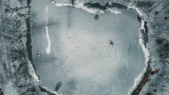 Drone looking down towards a single player playing ice hockey on a frozen pond or lake in Canada.
