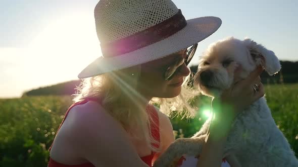 A woman kisses her dog on a sunset background.