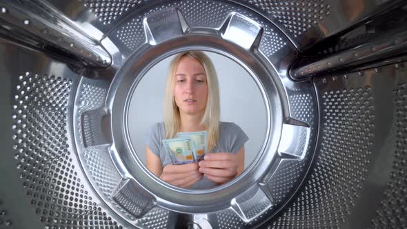 Young beautiful housewife counts dollars of money near washing machine.