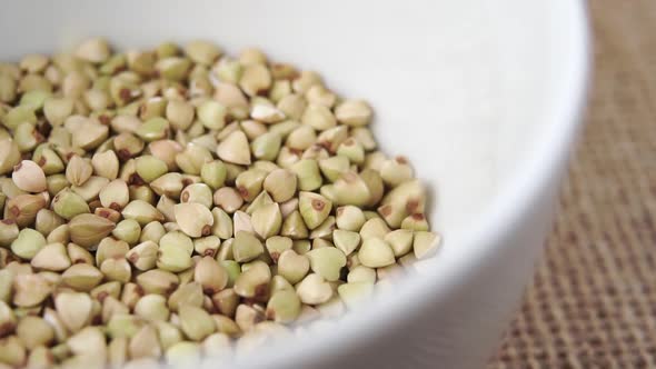 Macro shot falling green buckwheat seeds in a heap in a white bowl