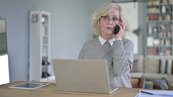 Professional Old Woman Working on Laptop and Talking on Smartphone