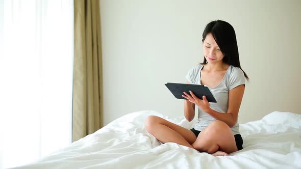 Woman using digital tablet computer and and sitting on bed