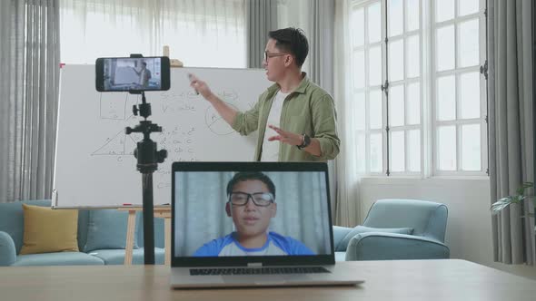 Asian Male Teacher Teaching Math Online At Home With Boy Student On Laptop Screen