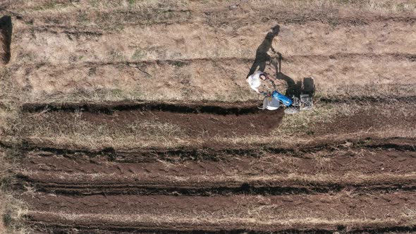 AERIAL - Man working a field with a rototiller, agriculture in Sweden, wide shot