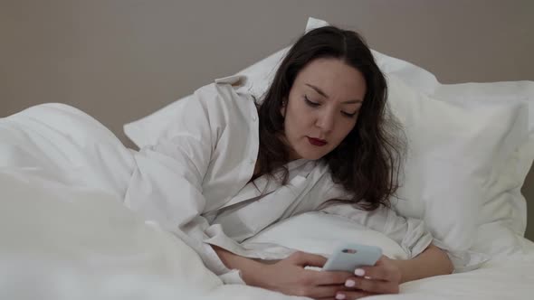 Young Woman Is Chatting By Messenger App in Smartphone at Morning Lying in Bed After Wake Up