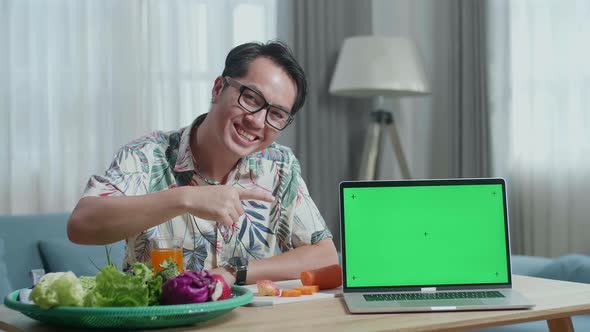 Man Pointing Green Screen Laptop On The Table And Smiling To Camera While Preparing Healthy Food