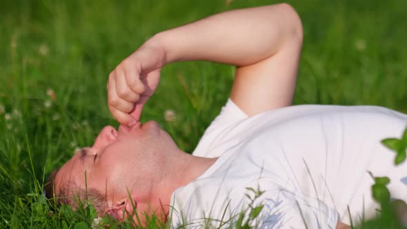 The Man is Resting in the Orchard He is Lying on the Grass and Eating Strawberries