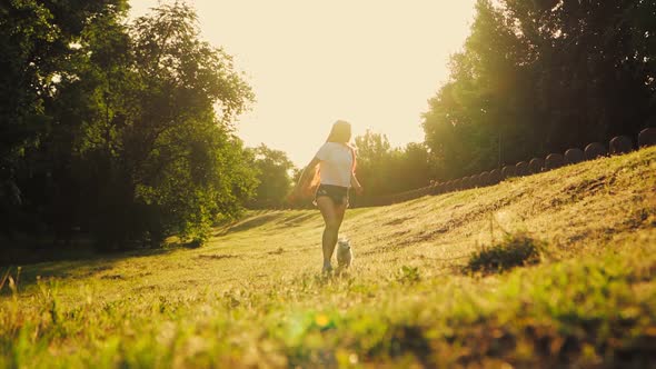 Happy Woman Playing With Two Dog In The Park. Beautiful Girl Runs with a Puppy during Sunset