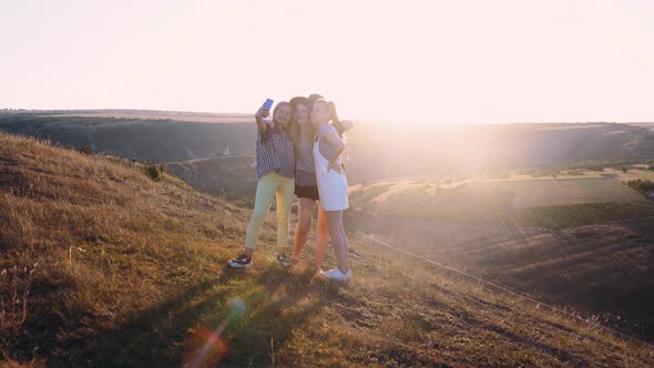 A Group of Three Girls Filming a Video Blog Sitting on a Cliff in the Mountains