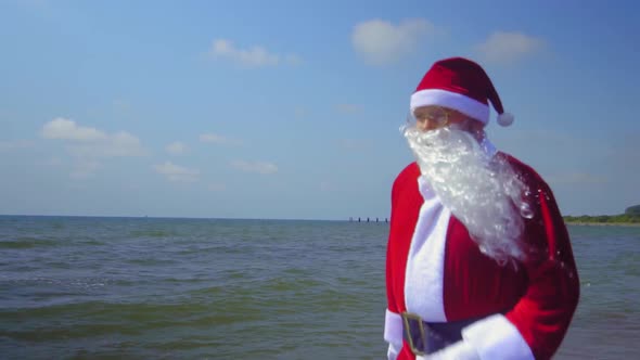 Santa Claus in costume walks along sandy shore of sea