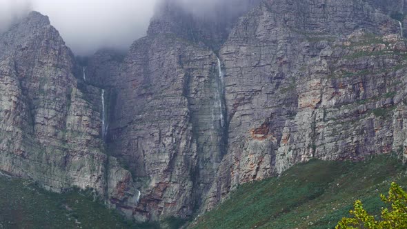 Multiple waterfalls falling down mountain side after heavy rains, zoomed-in panning shot