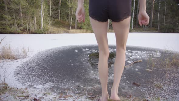 A young woman approaches an ice hole and steps in with one foot